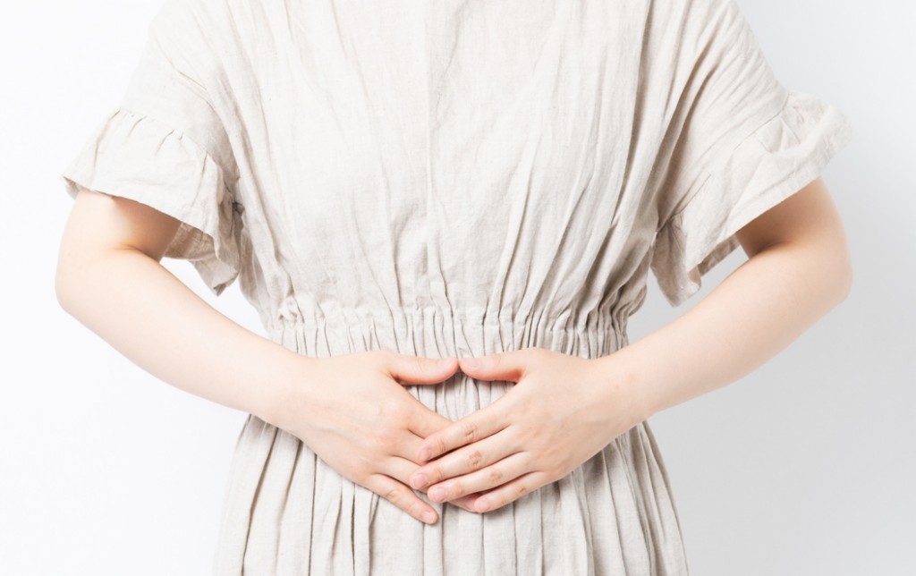明るい背景の前で、下腹部に手を添えている様子。不妊のイメージ。